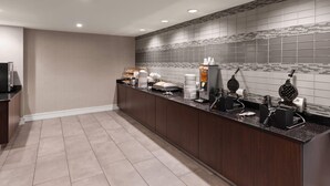 Ein moderner Küchenbereich mit einer langen Arbeitsplatte, einem Waffeleisen, einer Kaffeestation und einer gefliesten Spritzschutzwand.