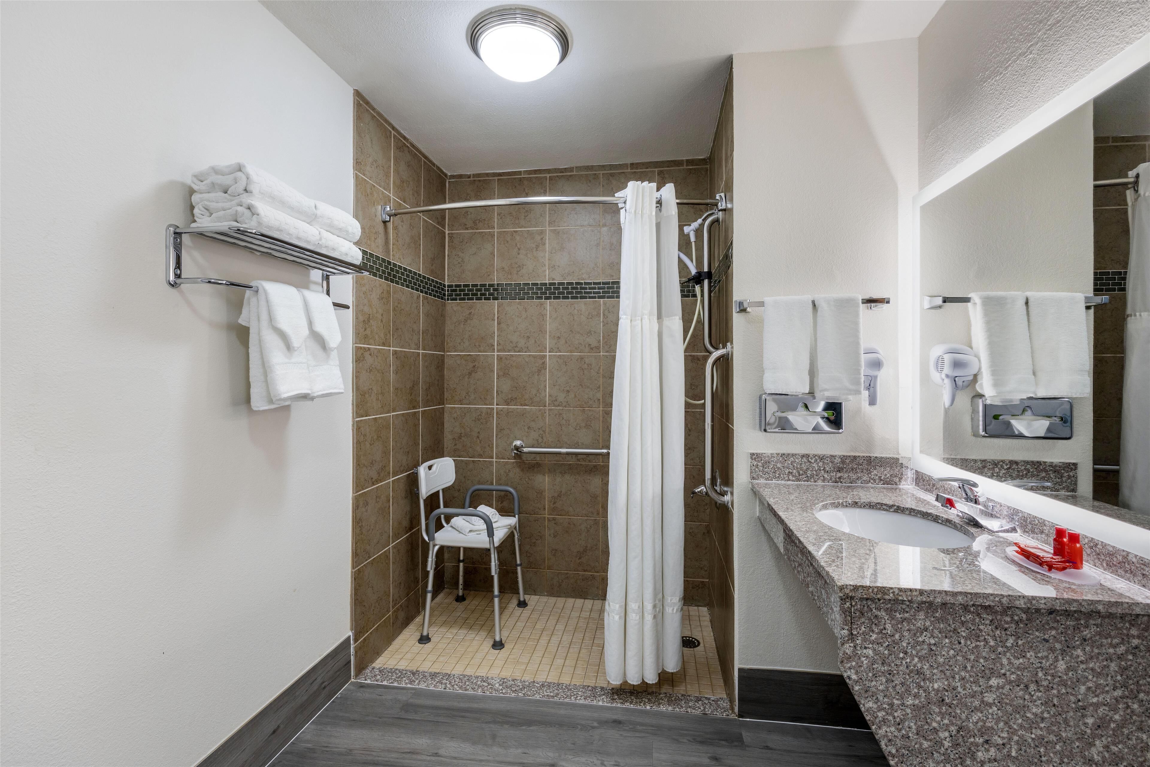 A modern bathroom with a shower, a wheelchair-accessible chair, a sink, and a vanity with a mirror.