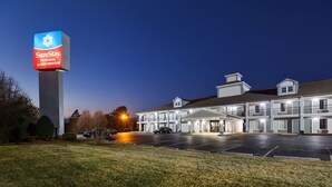 Un motel con un letrero grande, varias habitaciones y un estacionamiento.