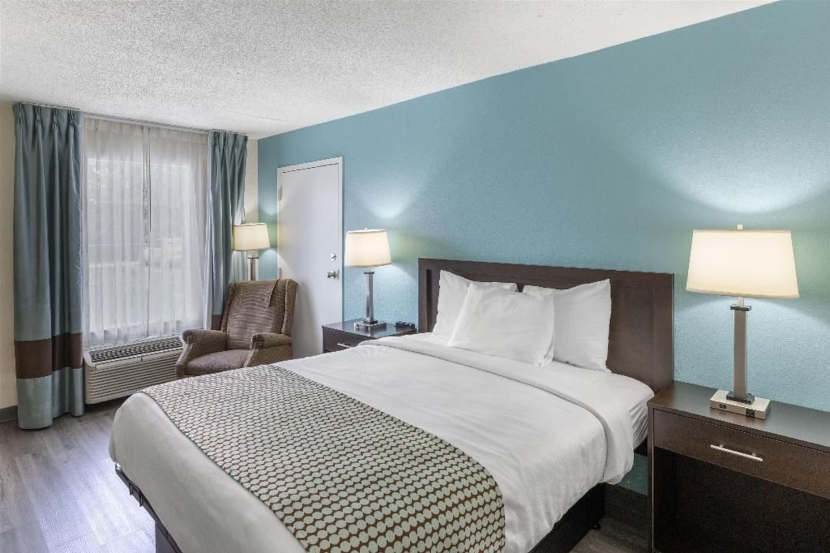 A hotel room with a large bed, two bedside tables with lamps, a chair, and a window with curtains.