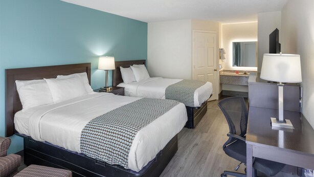 Habitación de hotel con dos camas, un escritorio, una silla y un baño visible a través de una puerta abierta.