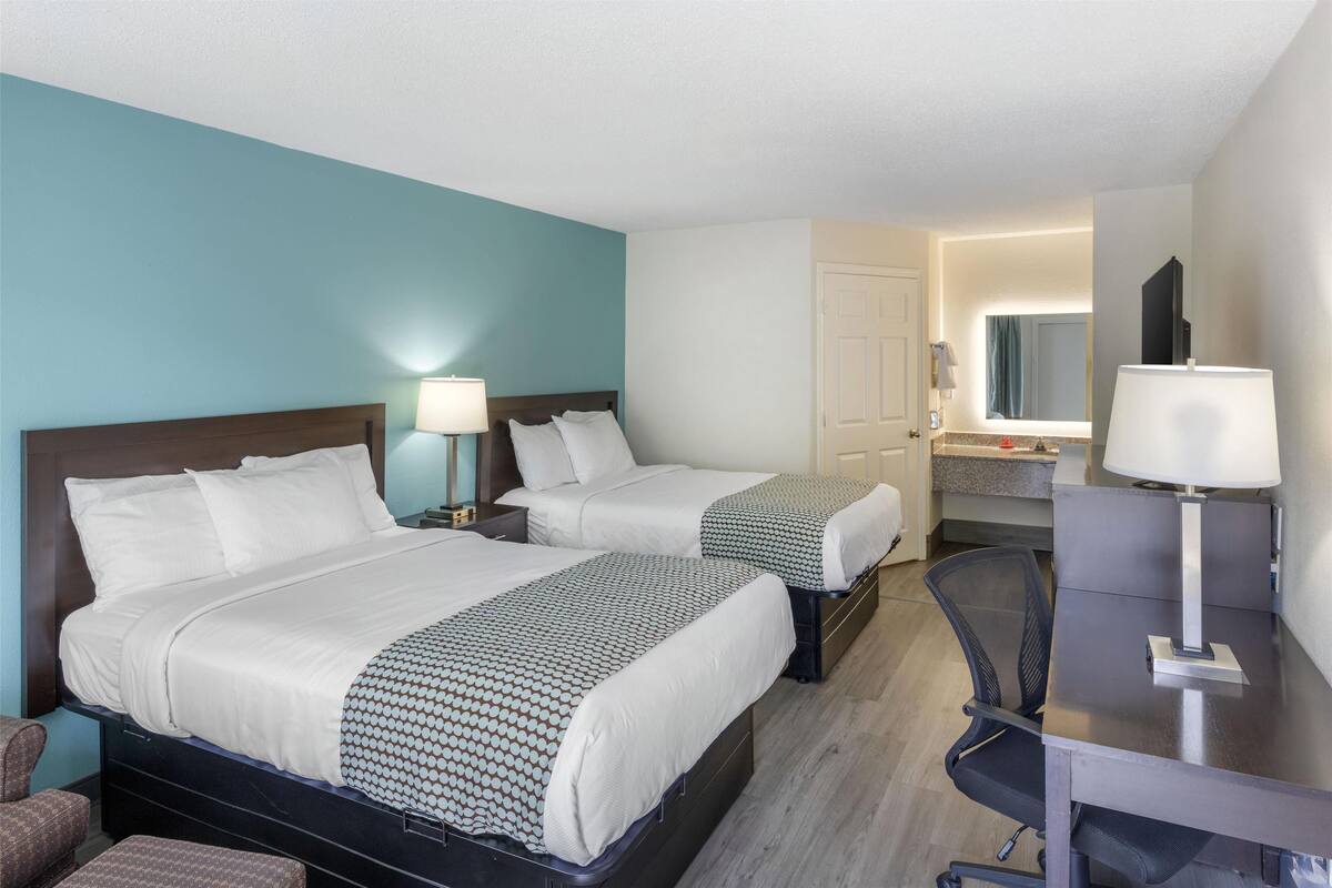 Hotelkamer met twee bedden, een bureau, een stoel en een badkamer door een geopende deur zichtbaar.