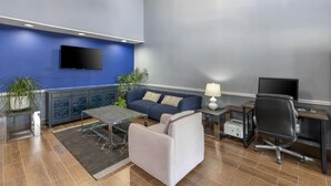 Una sala de estar moderna con una pared azul de acento, un sofá, una mesa de centro, un escritorio con una computadora y un televisor montado en la pared.