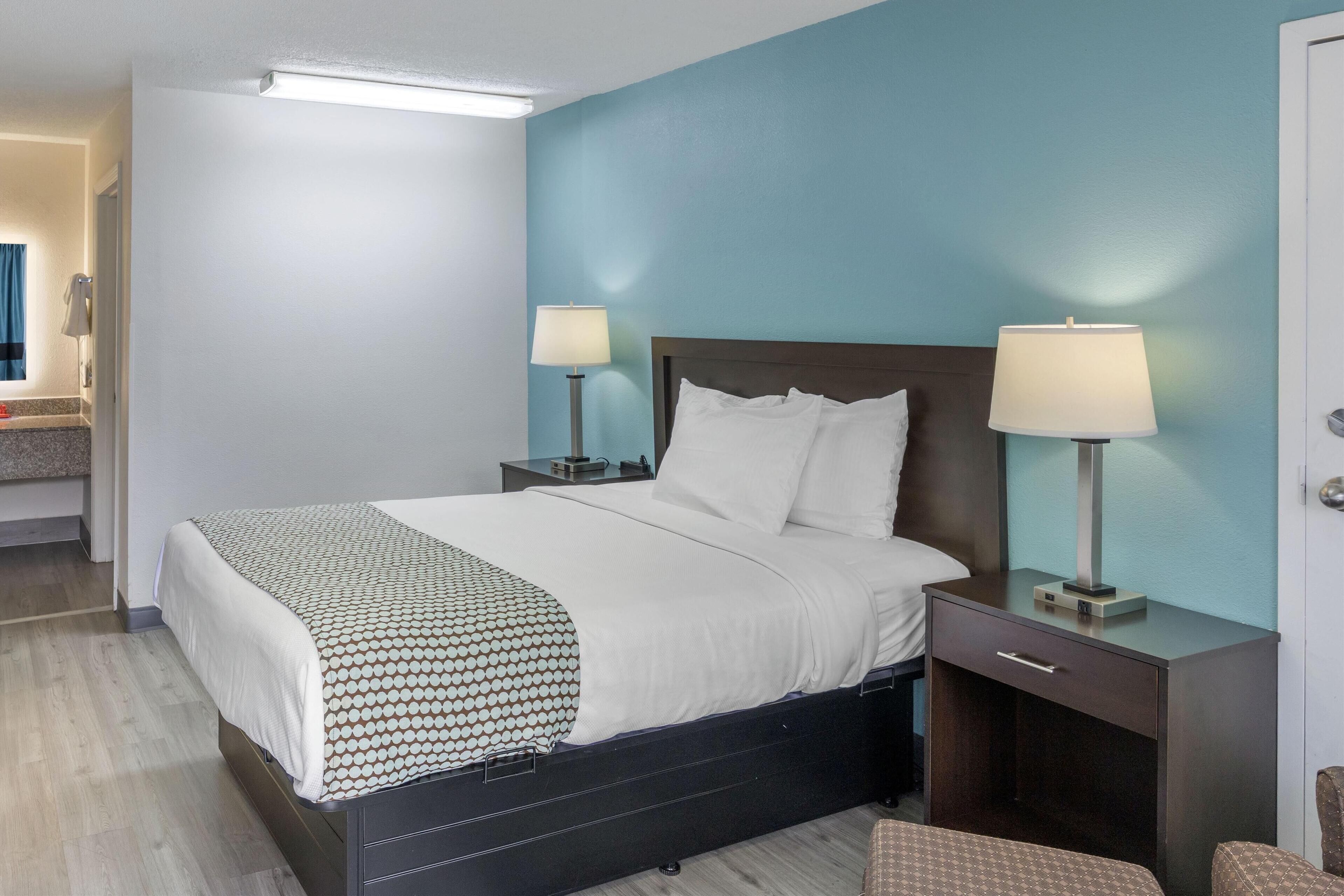 A hotel room with a bed, bedside tables with lamps, a nightstand, and a chair.