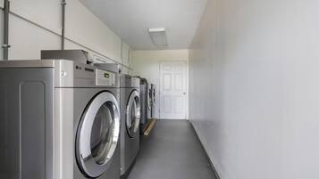 Une buanderie équipée de plusieurs lave-linge et sèche-linge LG, une porte blanche au fond et un sol de couleur claire.