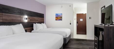 Quarto de hotel com duas camas, um ventilador de teto, um quadro na parede, uma porta e uma TV em um armário.