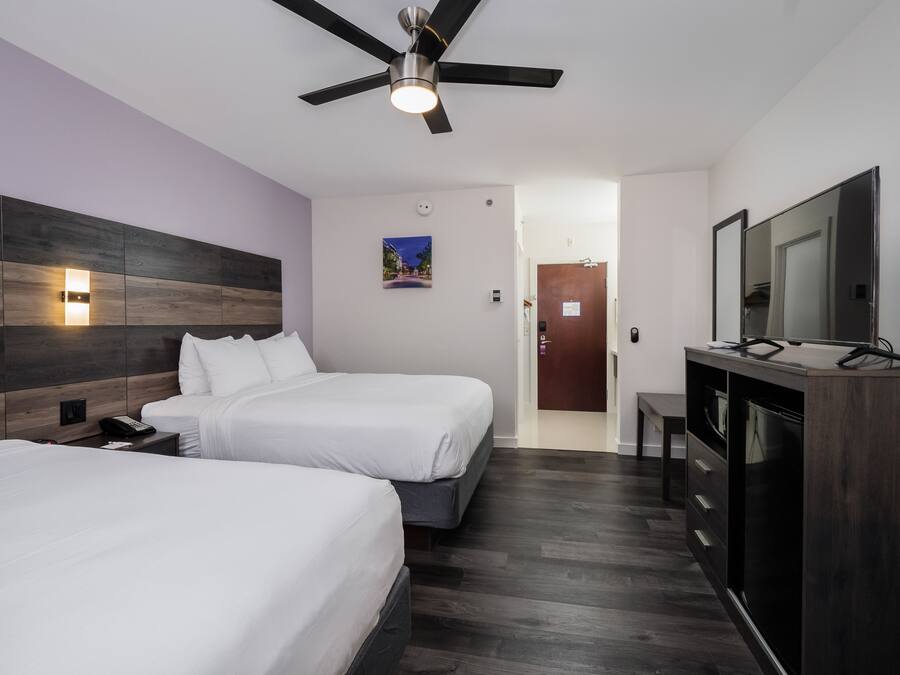 A hotel room with two beds, a ceiling fan, a TV, and a wooden headboard.