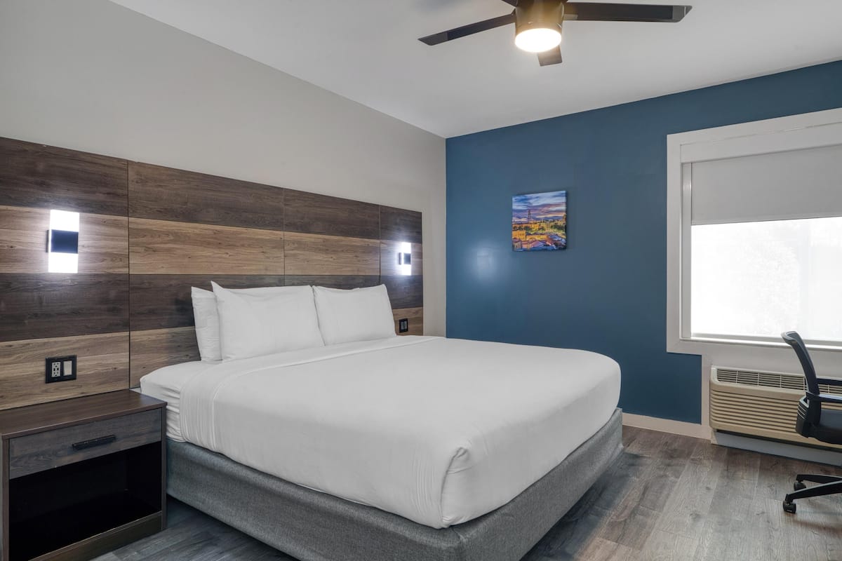 A modern bedroom with a bed, a nightstand, a ceiling fan, and a window with blinds.