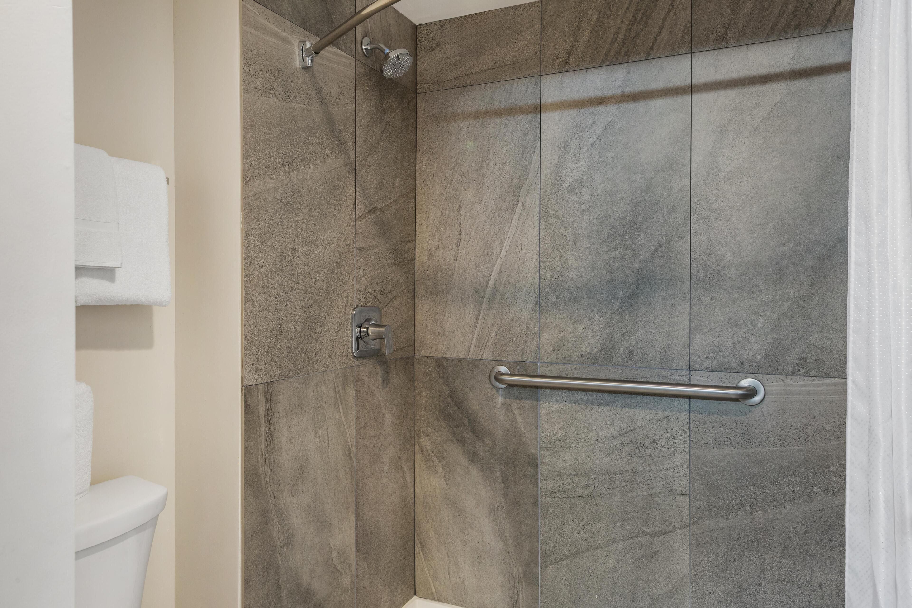 A shower with a handrail, a towel rack, and a toilet.