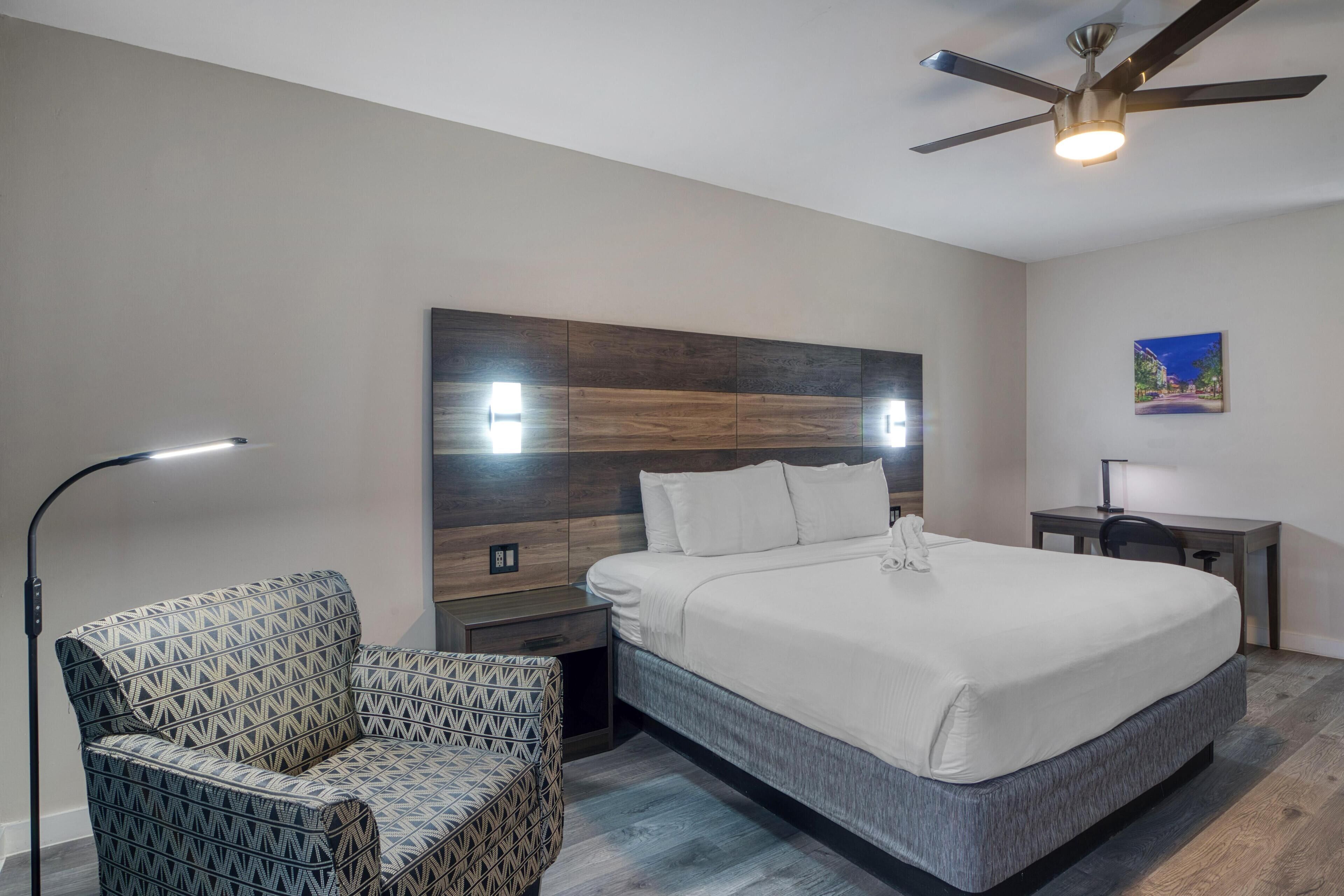 Una camera d'albergo moderna con un letto grande, una poltrona con motivi decorativi, una scrivania e una ventola a soffitto.