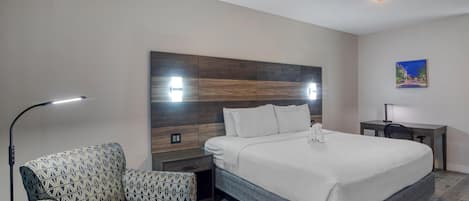 Una camera d'albergo moderna con un letto grande, una poltrona con motivi decorativi, una scrivania e una ventola a soffitto.