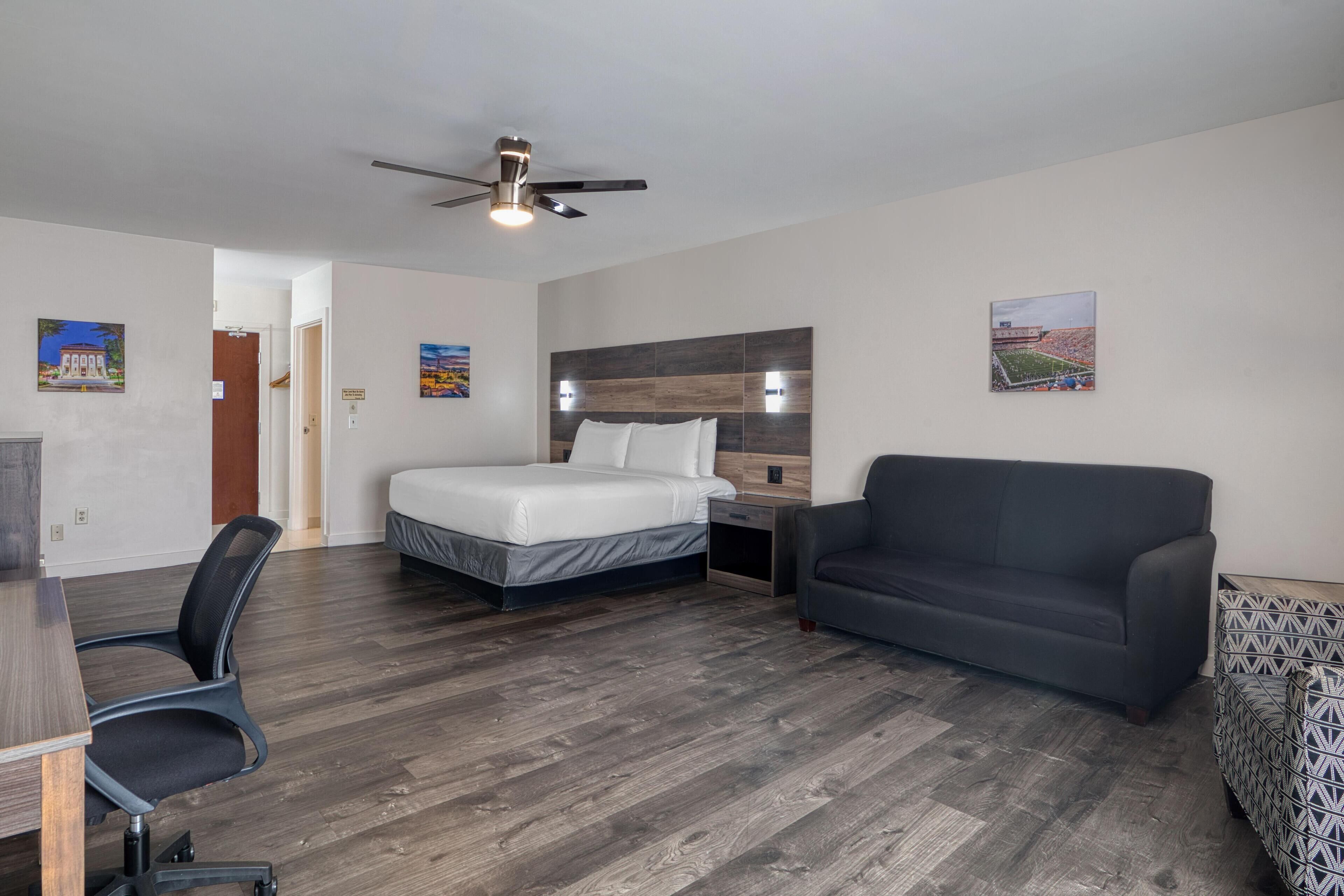 Una habitación de hotel con cama, escritorio, silla, sofá y ventilador de techo.
