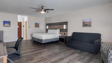 Una habitación de hotel con cama, escritorio, silla, sofá y ventilador de techo.