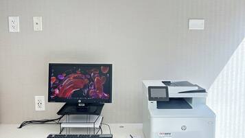 A modern office desk with a desktop computer, a printer, and a security camera on the ceiling.