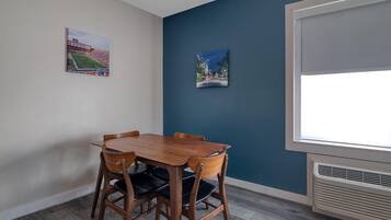 A dining area with a wooden table and chairs, two framed pictures on the wall, and a window with blinds.