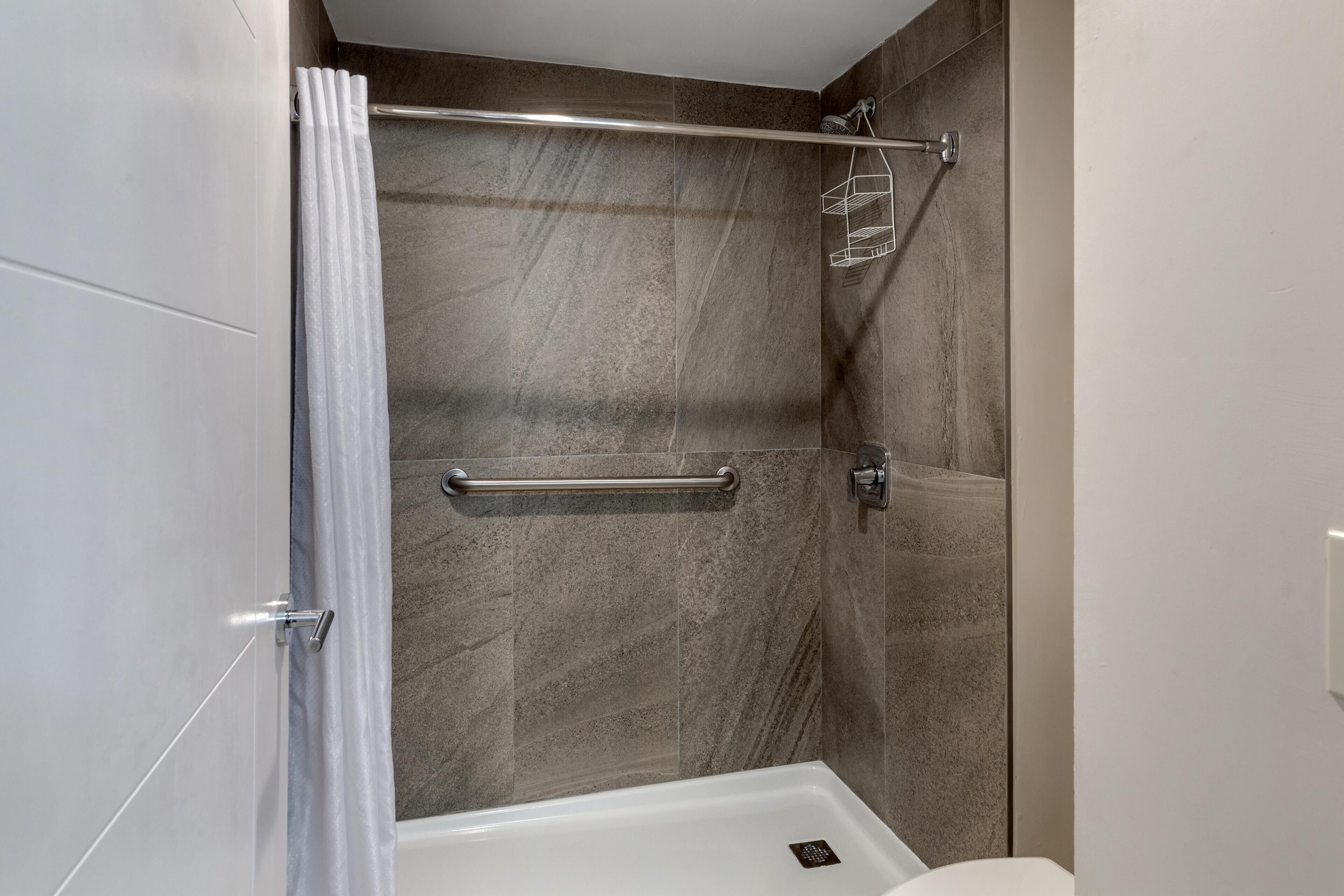 A modern bathroom with a shower area, a grab bar, and a white bathtub.