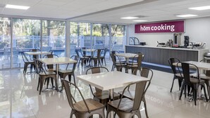 A modern dining area with tables and chairs, a kitchen counter, and a sign reading "höm cooking". - HOM Hotel Gainesville, SureStay Collection by Best Western (Gainesville)