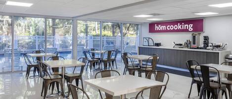 Un comedor moderno con mesas y sillas, una encimera de cocina y un letrero que dice "höm cooking".