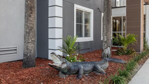 A modern building with a gray facade, a large window, and a landscaped area with a crocodile sculpture. - HOM Hotel Gainesville, SureStay Collection by Best Western (Gainesville)