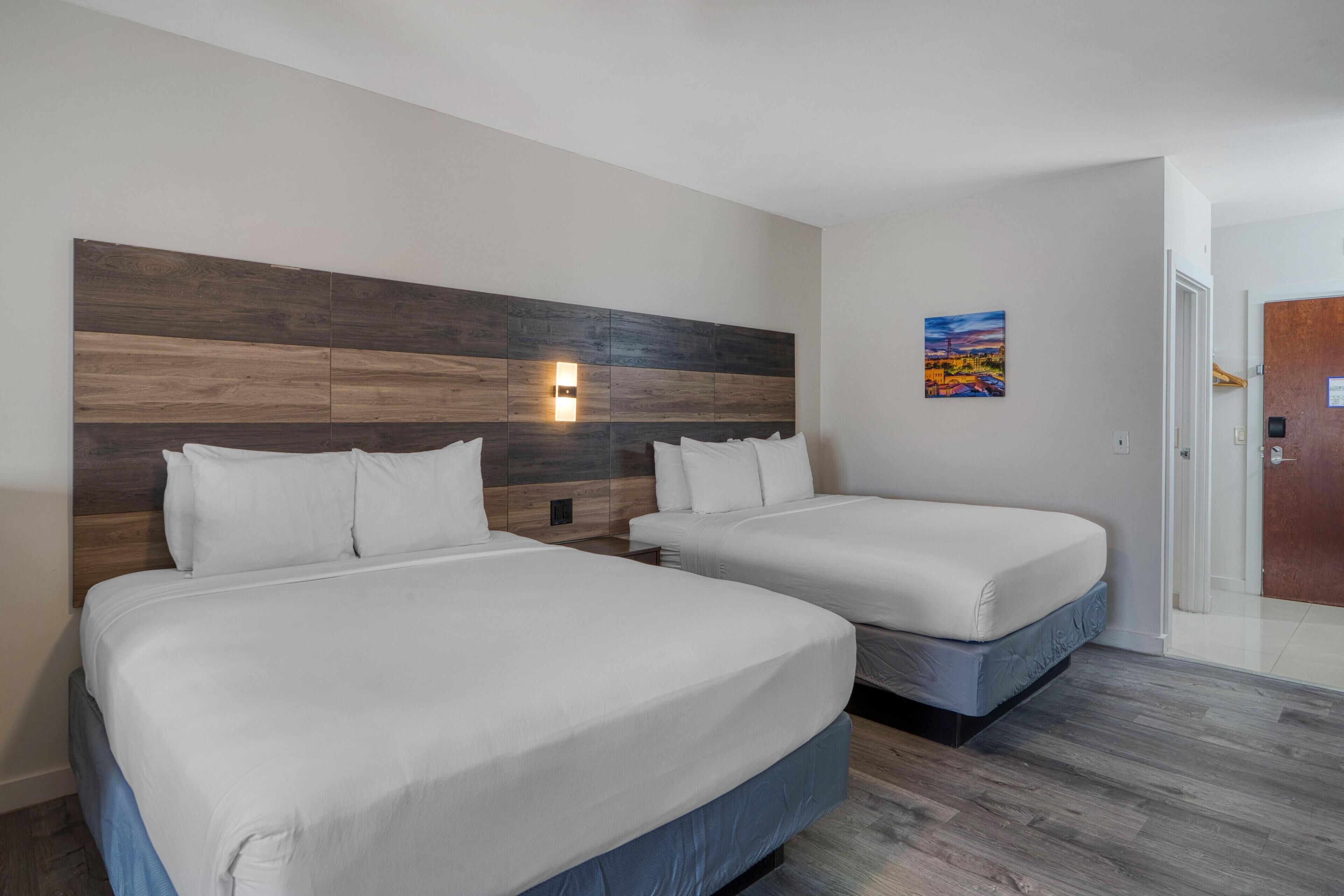 Habitación de hotel con dos camas, cabecero de madera, luz nocturna y un cuadro en la pared.