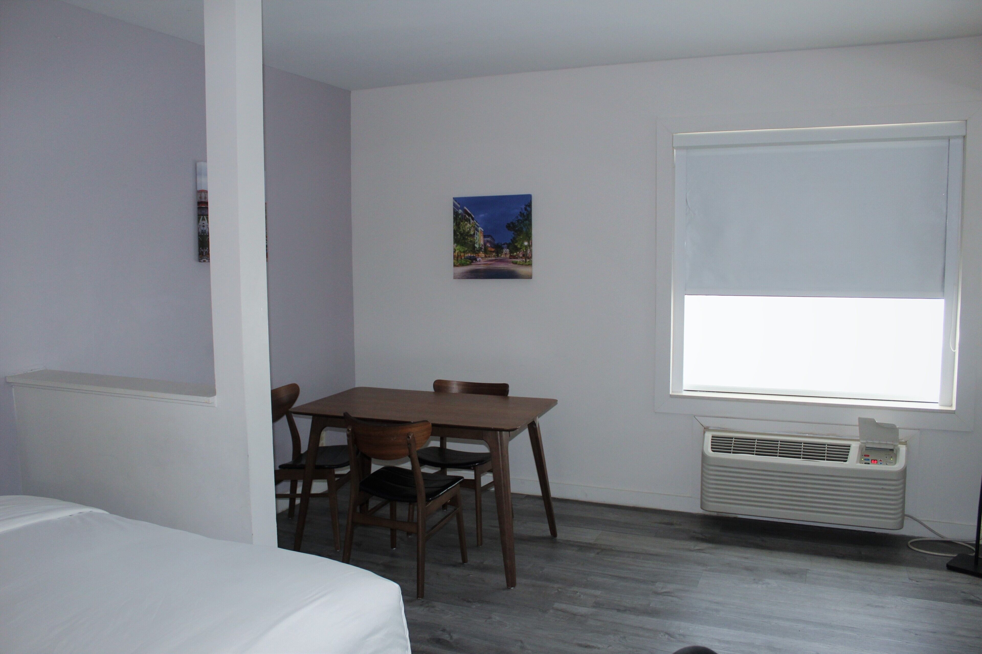 Una habitación con una cama, una mesa de comedor con sillas, una ventana con persianas y un aire acondicionado instalado en la pared.