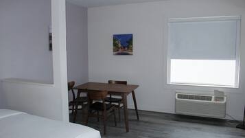 Una habitación con una cama, una mesa de comedor con sillas, una ventana con persianas y un aire acondicionado instalado en la pared.