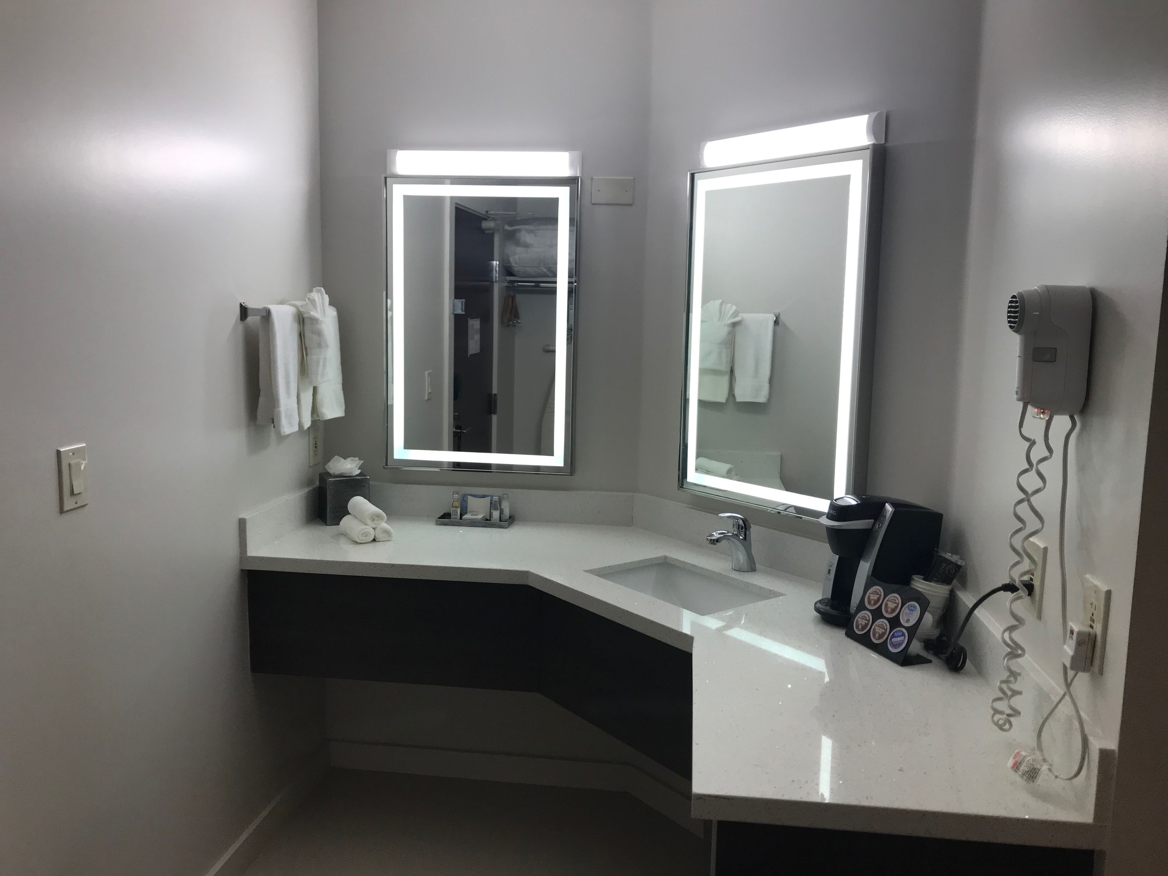 A modern bathroom with two sinks, a large mirror with integrated lighting, a hairdryer, and neatly arranged towels.