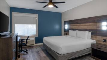 A bedroom with a bed, desk, chair, and a ceiling fan.