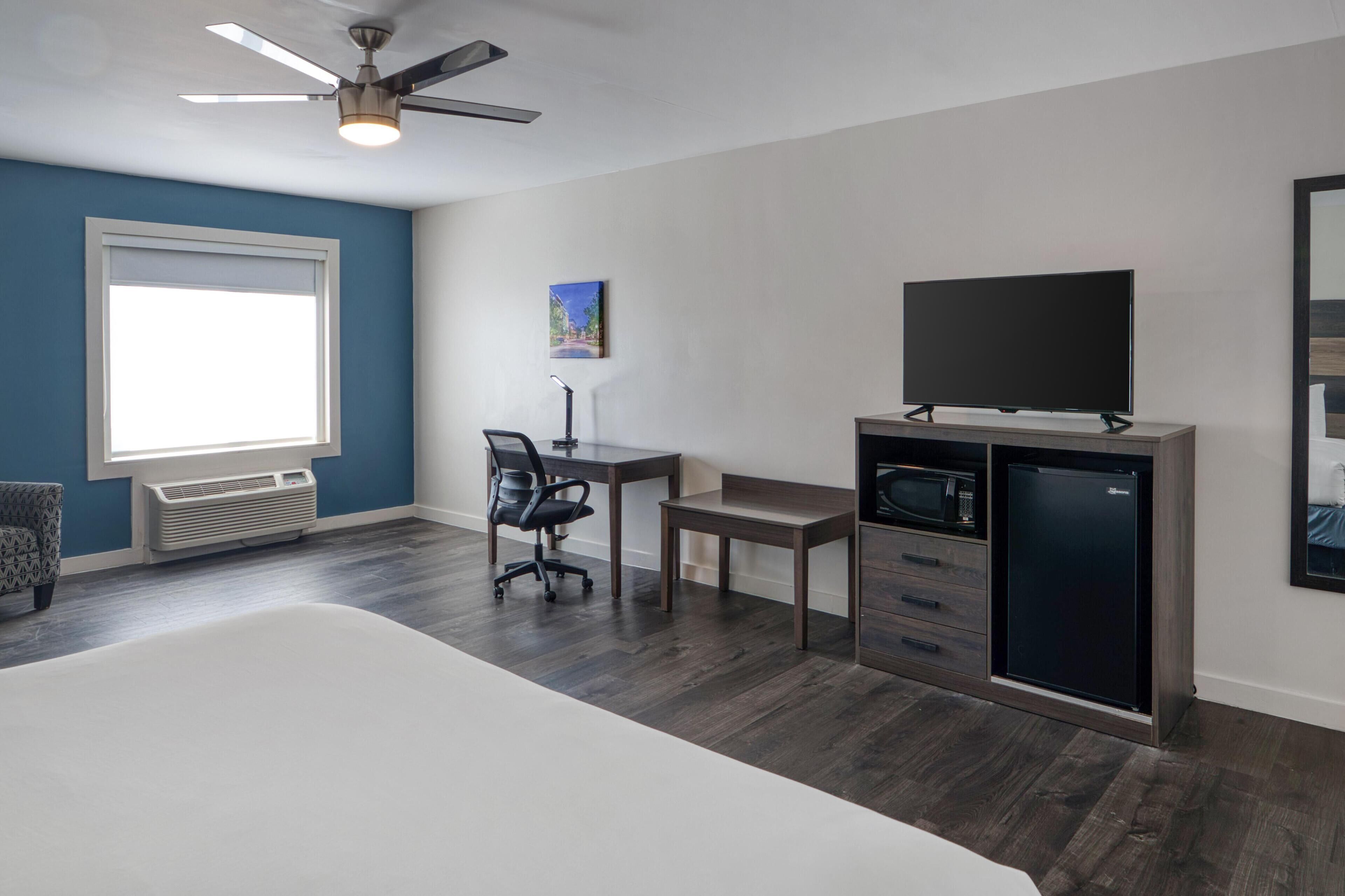 A bedroom with a bed, a desk, a chair, a television, a microwave, and a refrigerator.