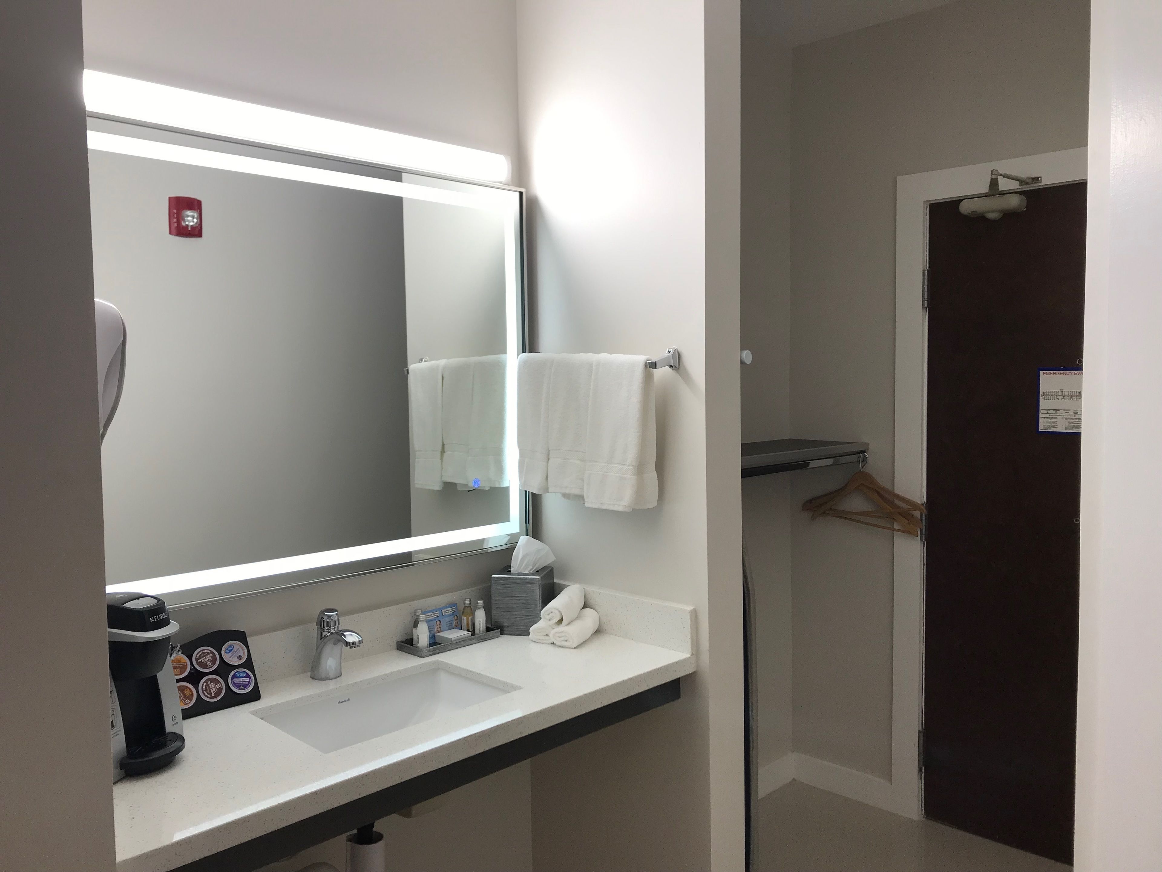 A modern bathroom with a large mirror, a sink, a coffee maker, and a towel rack.