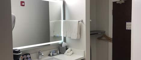 A modern bathroom with a large mirror, a sink, a coffee maker, and a towel rack.