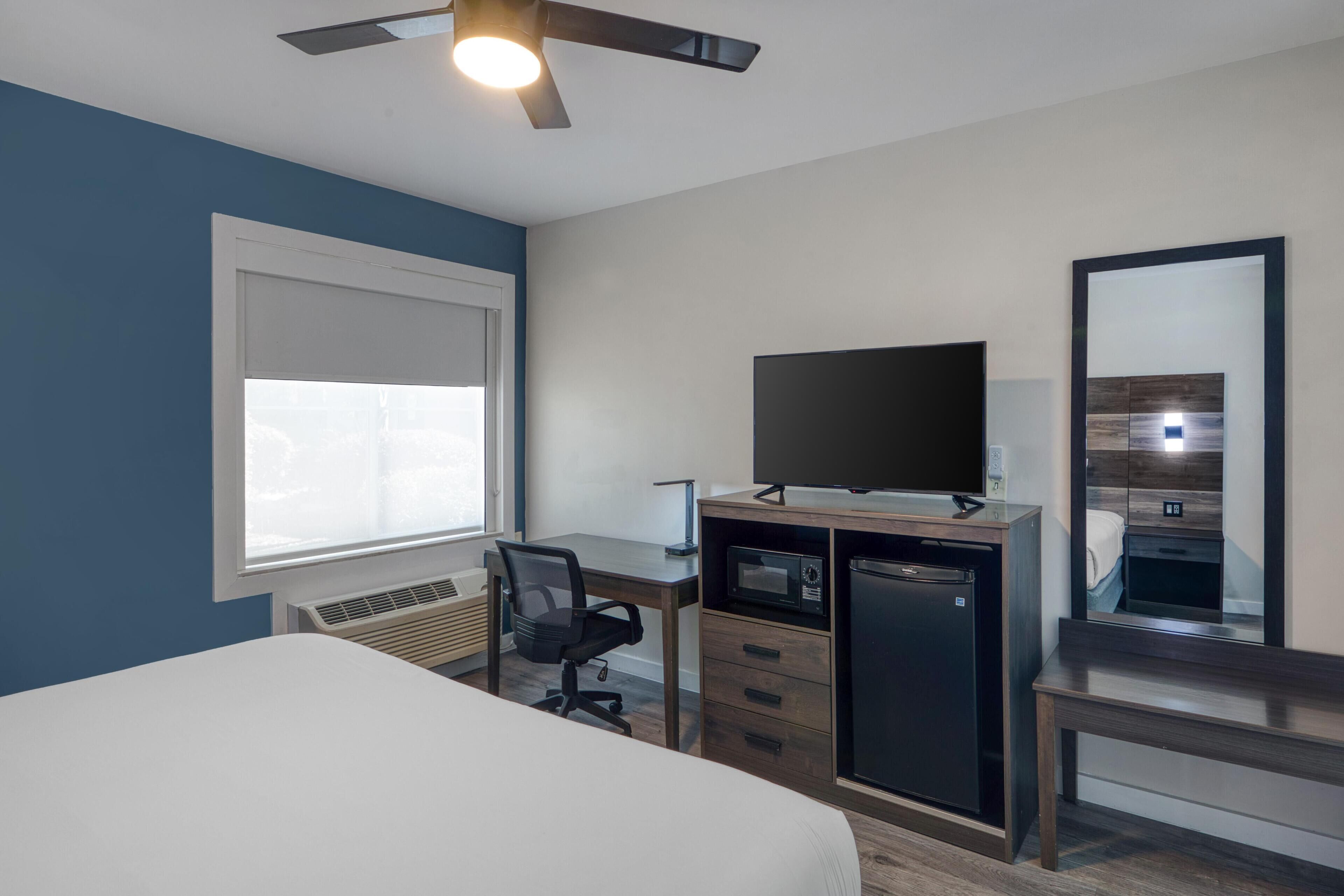 A bedroom with a bed, a desk, a chair, a television, a microwave, and a refrigerator.