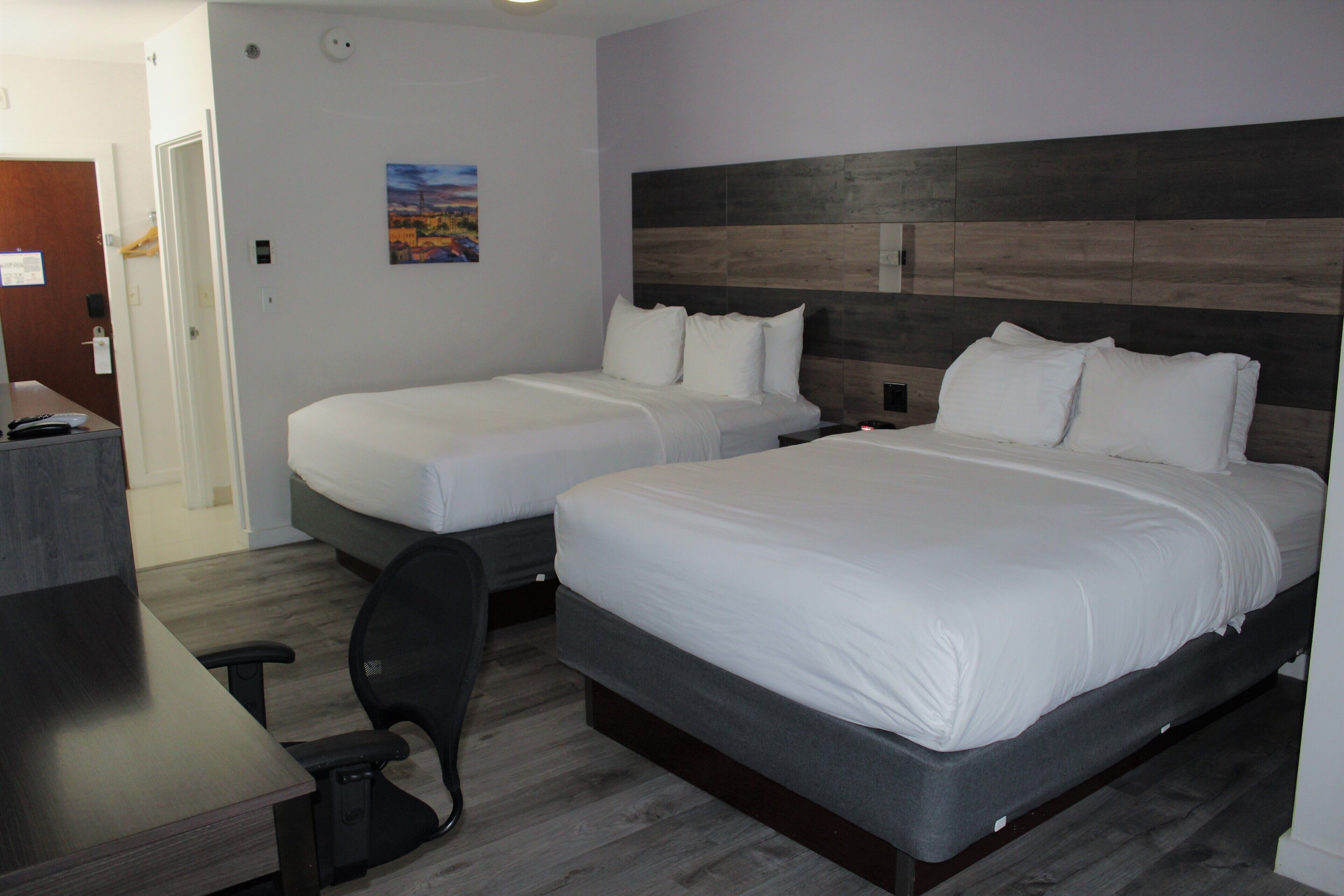 A hotel room with two beds, a desk, and a chair.