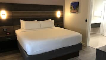 Una cama bien hecha con sábanas blancas, un cabecero de madera y dos lámparas de lectura fijadas a la pared.