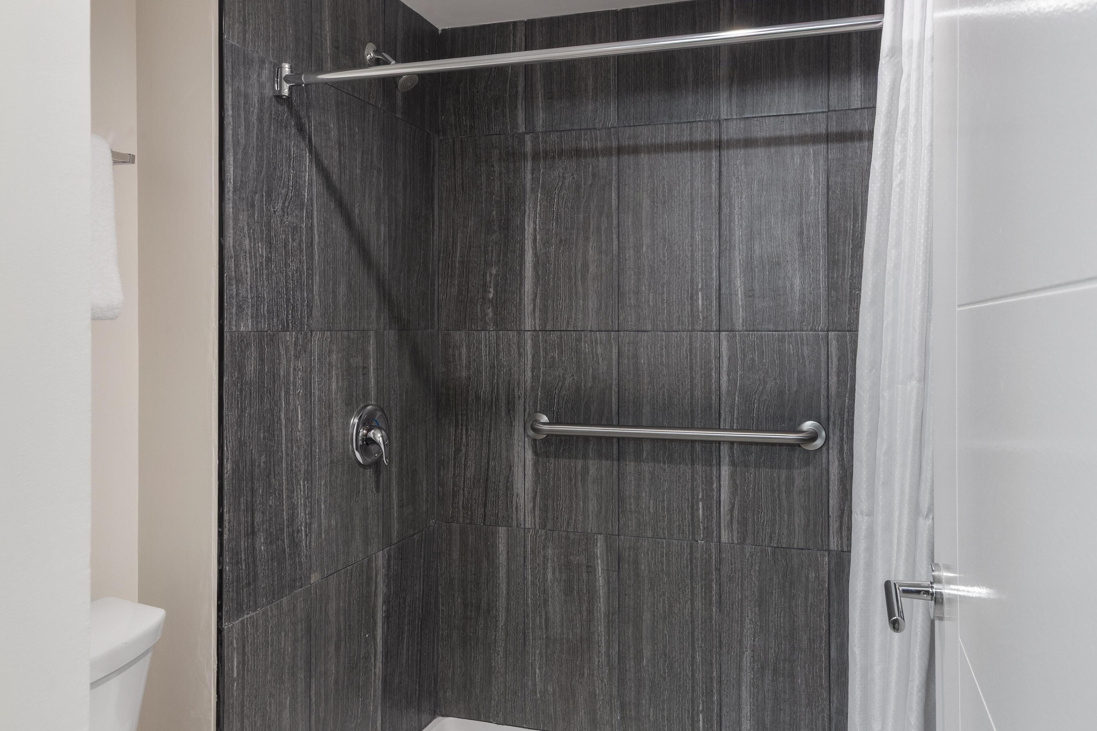 A shower area with dark tiled walls, a glass door, and a metal grab bar.