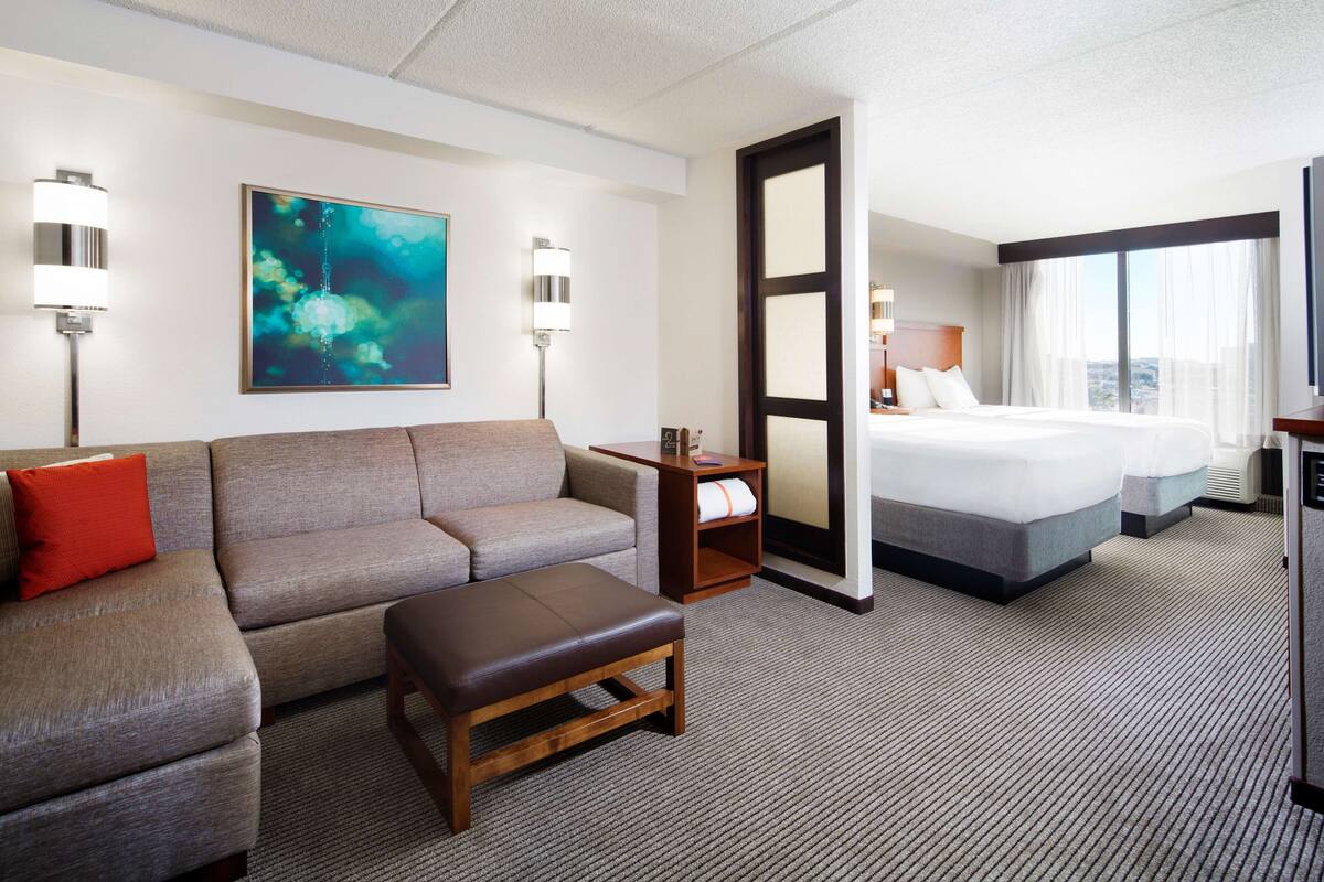 A hotel room with a sofa, a small table, a bed, and a large window.