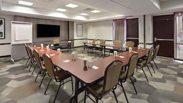 Un salón de conferencias con una gran mesa, sillas, una pantalla de proyector y una pizarra.