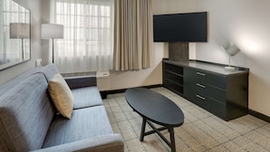 Une chambre d’hôtel moderne équipée d’un canapé, d’une petite table, d’un téléviseur à écran plat, d’un bureau avec des tiroirs et d’une lampe.