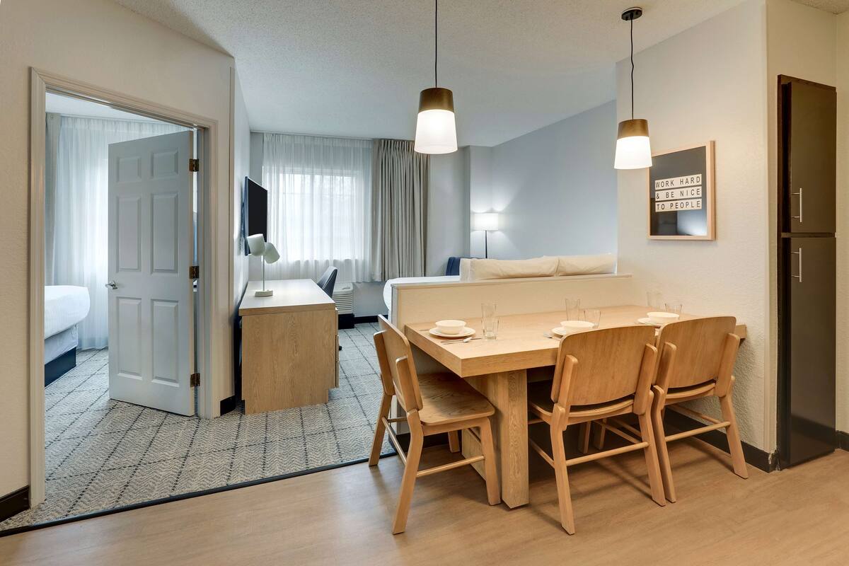 A hotel room with a dining area, a bed, a desk, and a wardrobe.