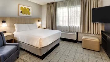 Quarto de hotel com uma cama grande, uma escrivaninha, uma cadeira, uma televisão e uma janela com cortinas.