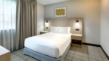 A hotel room with a large bed, two bedside tables, a headboard with a light fixture, and a framed picture on the wall.