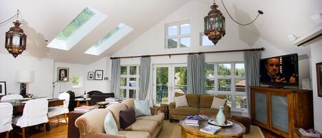 A spacious living room with a high ceiling, large windows, a television, and a dining area.