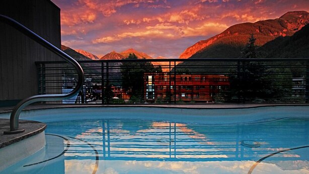 A swimming pool with a view of mountains and a building in the background. - Camel's Garden Hotel (Telluride)
