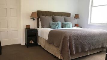 Un dormitorio con cama, mesitas de noche, lámpara, ventana y puerta.