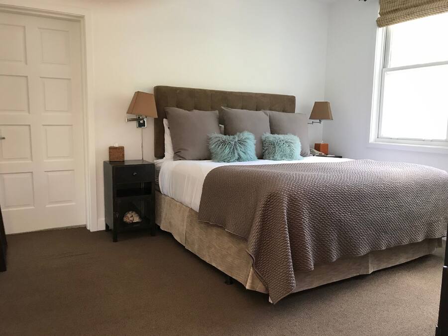 Un dormitorio con cama, mesitas de noche, lámpara, ventana y puerta.