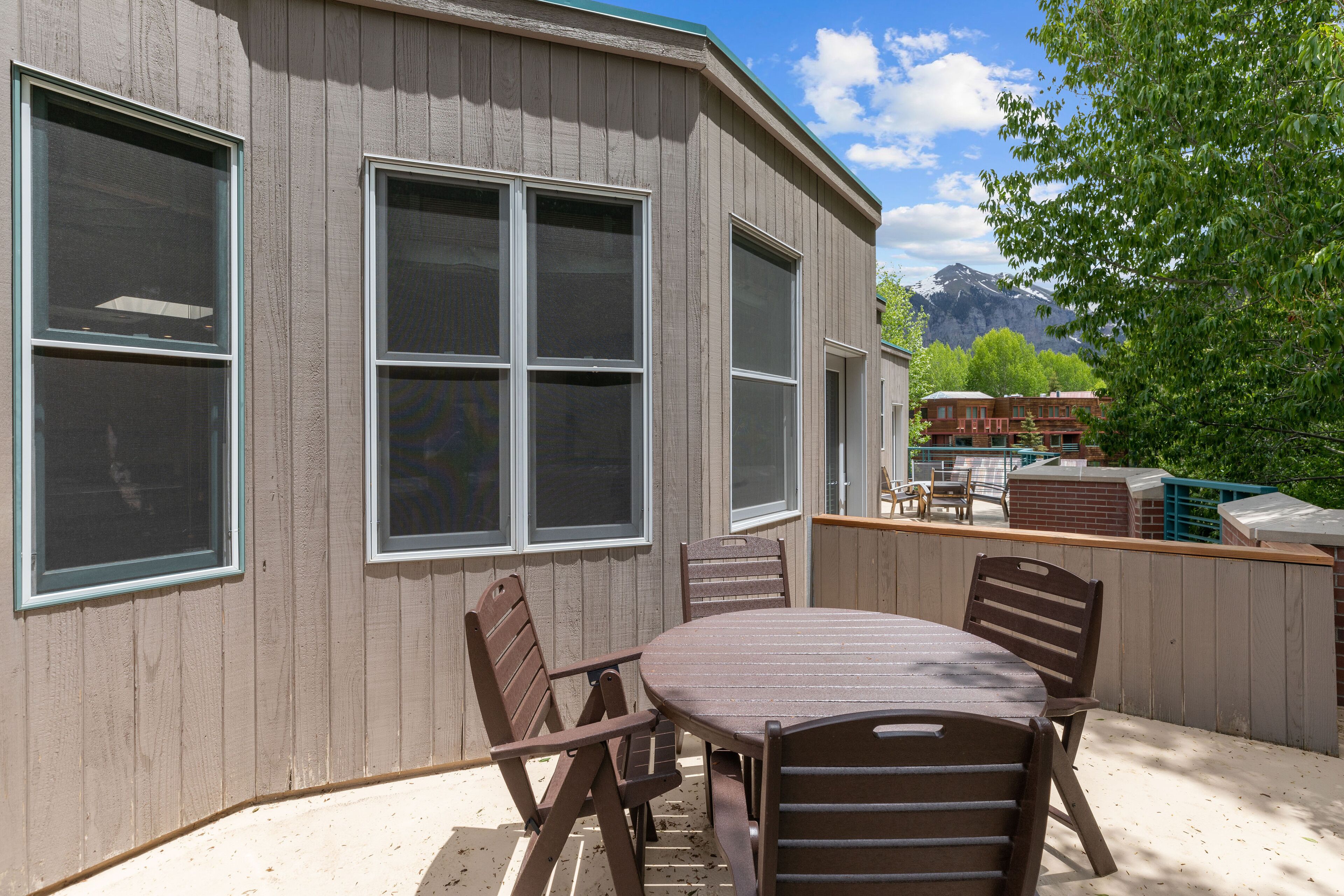 A patio with a table and chairs, large windows, and a view of mountains.