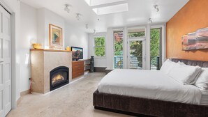 A bedroom with a fireplace, a large bed, and a balcony with a view of greenery. - Camel's Garden Hotel (Telluride)