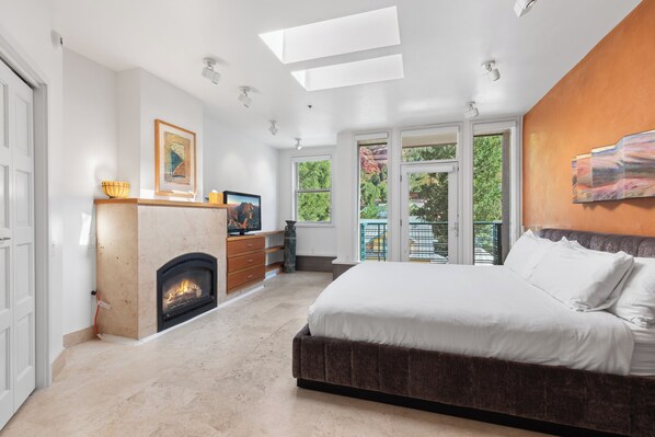 A bedroom with a fireplace, a large bed, and a balcony with a view of greenery. - Camel's Garden Hotel (Telluride)