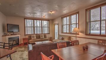 A spacious living room with a fireplace, large windows, a dining table, and comfortable seating.