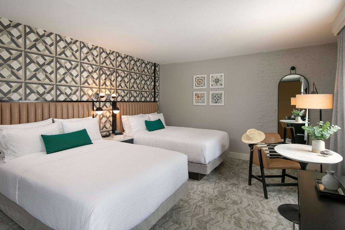 Ein Hotelzimmer mit zwei Betten, einem Schreibtisch, einem Stuhl und einem Spiegel.